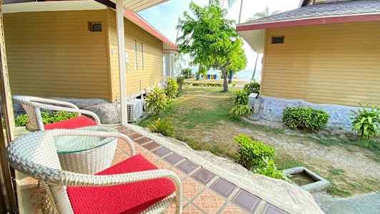 To stole med røde hynder på en veranda med udsigt over have og hav. (AI-genereret tekst)