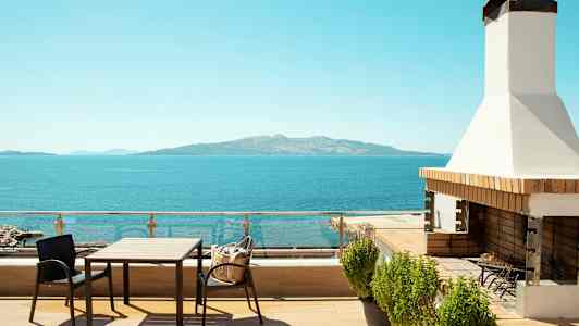 En terrasse med bord, stole og grill med udsigt over havet og en fjern ø. (AI-genereret tekst)