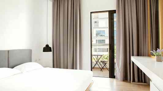 Et moderne soveværelse med en stor seng, grå gardiner og en dør der fører ud til en altan udenfor. (AI-genereret tekst)