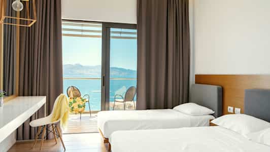 Hotelværelse med to enkeltsenge og adgang til en balkon med udsigt over havet. (AI-genereret tekst)