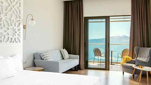 Hotelværelse med seng, sofa, lænestol og altan med havudsigt. (AI-genereret tekst)