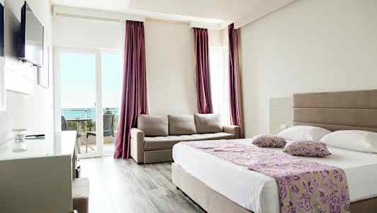 Et hotelværelse med en dobbeltseng, en sofa og en balkon med udsigt over havet. (AI-genereret tekst)