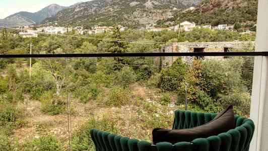 Udsigt fra altanen mod en grøn dal med træer, buske og bygninger i baggrunden. (AI-genereret tekst)