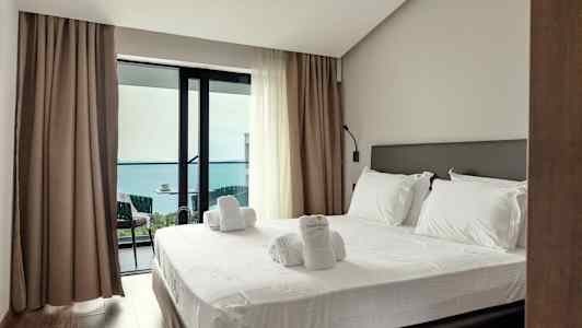 Et hotelværelse med en opredt seng og adgang til en balkon med havudsigt. (AI-genereret tekst)