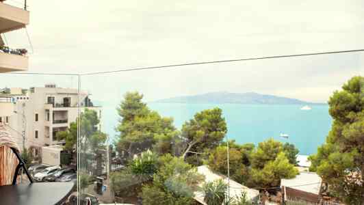 Udsigt fra en altan mod havet og frodige træer. (AI-genereret tekst)