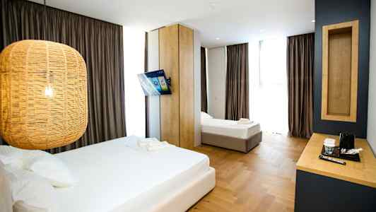 Et hotelværelse med to senge, en hængende lampe, et vægmonteret tv og et skrivebord med en kaffemaskine. (AI-genereret tekst)