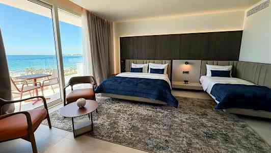 Et hotelværelse med to senge og en balkon med havudsigt. (AI-genereret tekst)