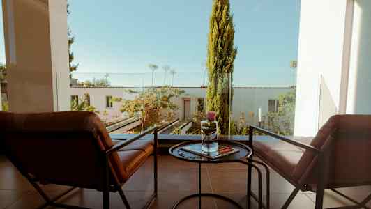 To stole og et lille bord på en balkon med udsigt over en frodig have. (AI-genereret tekst)