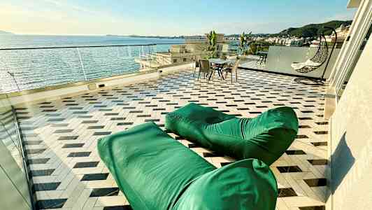 En terrasse med havudsigt, grønne sækkestole, et bord med stole og en hængestol. (AI-genereret tekst)