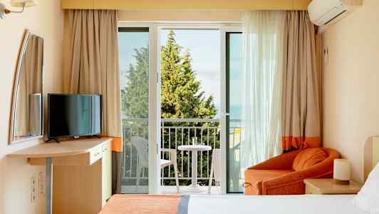 Et hotelværelse med altan, seng, lænestol og TV. (AI-genereret tekst)