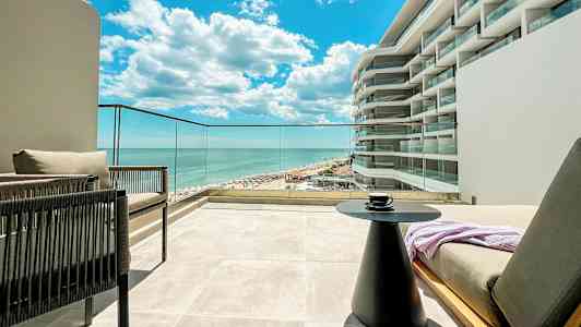 Udsigt fra en terrasse mod havet og en del af en bygning med moderne design. (AI-genereret tekst)