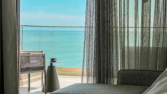 Udsigt fra et rum med glasdøre, der fører ud til en altan med havudsigt. En kop står på et bord. (AI-genereret tekst)