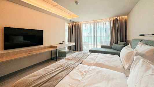 Et moderne hotelværelse med en dobbeltseng, vægmonteret TV, skrivebord og siddeområde ved store vinduer. (AI-genereret tekst)