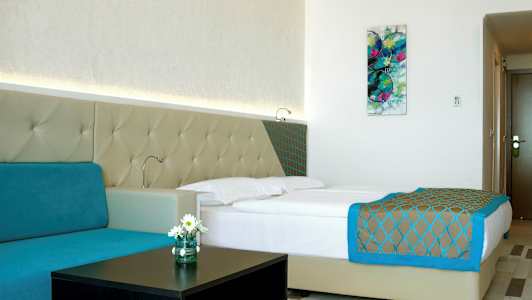 Et moderne hotelværelse med en dobbeltseng, turkis sofa og vægkunst. (AI-genereret tekst)