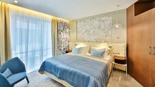 Et hotelværelse med en dobbeltseng, blåt sengetæppe og dekorativ væg bag sengen. (AI-genereret tekst)