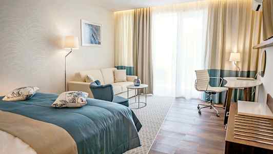 Et hotelværelse med en seng, sofa, bord og skrivebord med stol. (AI-genereret tekst)