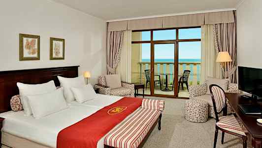 Et hotelværelse med dobbeltseng, siddeområde, et skrivebord og balkon med havudsigt. (AI-genereret tekst)