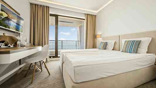 Hotelværelse med to senge, skrivebord og altan med havudsigt. (AI-genereret tekst)