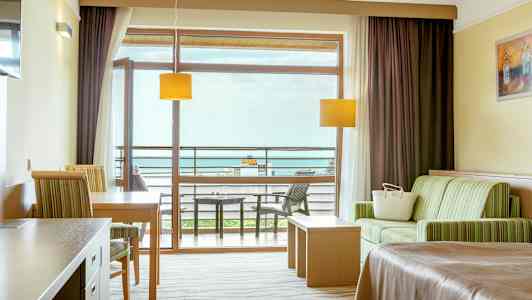 Et hotelværelse med siddeområde, bord, seng og altan med udsigt. (AI-genereret tekst)