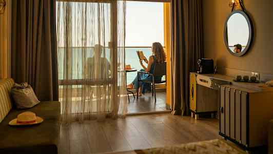 Hotelværelse med en altan, hvor en person sidder og læser med havudsigt. (AI-genereret tekst)