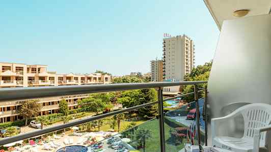 Lejlighedsbalkon med udsigt over poolområdet og hotelbygninger. (AI-genereret tekst)