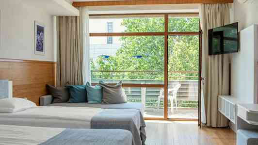 Et hotelværelse med to senge, en sofa med farverige puder og en glasdør, der fører til en altan. (AI-genereret tekst)