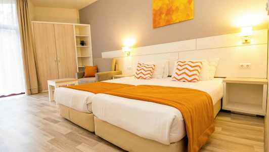 Et lyst hotelværelse med to senge, orange detaljer og møbler. (AI-genereret tekst)