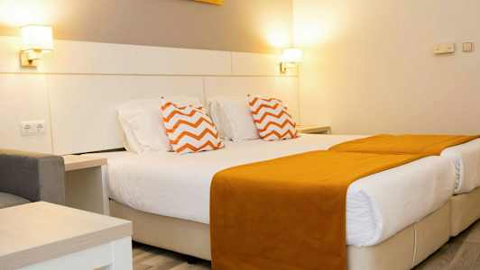 Et hotelværelse med to enkeltsenge med orange sengetæpper og pyntepuder med zigzagmønster. (AI-genereret tekst)