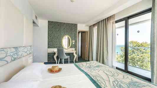 Hotelværelse med lyse møbler og store vinduer med udsigt over havet. (AI-genereret tekst)