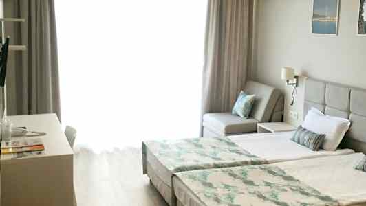 Lyst rum med to enkeltsenge, en sofa og skrivebord. (AI-genereret tekst)