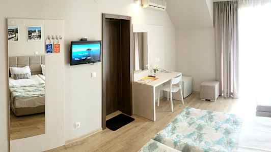 Et hotelværelse med to senge, et skrivebord, køleskab og et vægmonteret TV. (AI-genereret tekst)