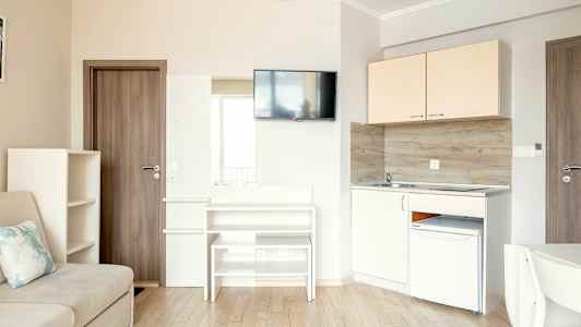 Et lille køkken- og opholdsrum med sofa, skabe, TV og køkkenudstyr. (AI-genereret tekst)