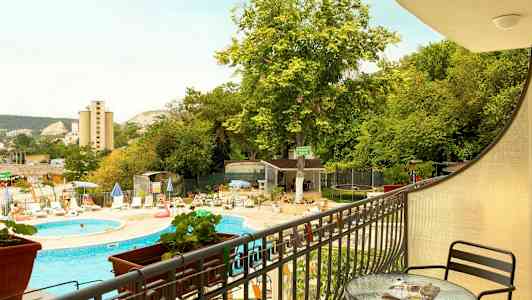 Udsigt fra en altan mod en udendørs pool, liggestole og grønne omgivelser. (AI-genereret tekst)