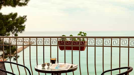 En altan med udsigt over havet, med et bord, stole og en altankasse. (AI-genereret tekst)