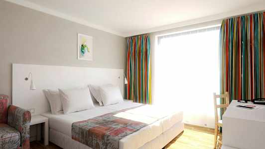 Et hotelværelse med en seng, et skrivebord og farverige gardiner. (AI-genereret tekst)