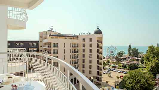 Udsigt fra en altan over et hotelområde med et pariserhjul og havet i baggrunden. (AI-genereret tekst)