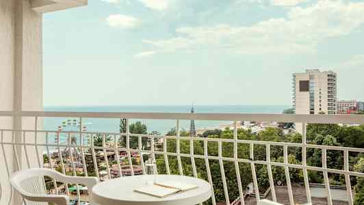 Udsigt fra altan med bord og to stole, hav og byer i baggrunden. (AI-genereret tekst)