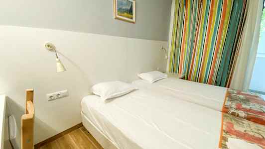 Et hotelværelse med to enkeltsenge, en lysegrå væg med et maleri ovenover, og farverige gardiner ved siden af. (AI-genereret tekst)