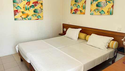 Et hotelværelse med to enkeltsenge, hvide sengelinned og farverige malerier på væggen. (AI-genereret tekst)