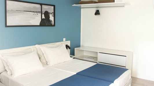 Hotelværelse med to enkeltsenge, hvide vægge og en blå bagvæg. (AI-genereret tekst)