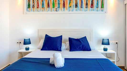 Billedet viser en seng med blå puder og sengetøj, flankeret af to natborde med blå lamper. (AI-genereret tekst)