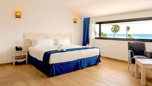 Et hotelværelse med en dobbeltseng og udsigt over havet gennem et stort vindue. (AI-genereret tekst)