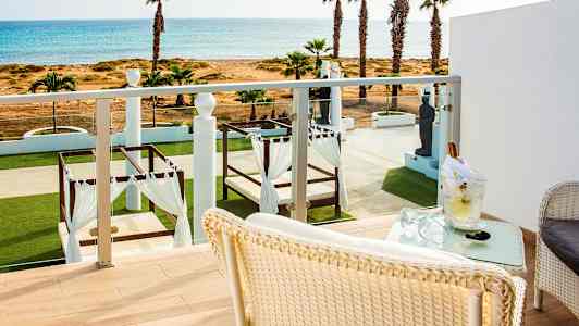 Udsigt fra en balkon over en frodig have med senge under baldakiner og havet i baggrunden. (AI-genereret tekst)