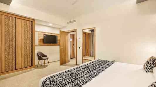 Et hotelværelse med en stor seng dekoreret med sort-hvidt mønster, trædetaljer i møbler og interiør, herunder garderober, døre og en tv-ramme. (AI-genereret tekst)