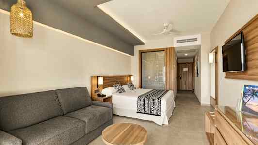 Et moderne hotelværelse med en seng, en sofa og et bord. Der er også et fladskærms-TV på væggen. (AI-genereret tekst)