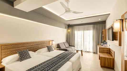 Et moderne hotelværelse med to senge, en sofa og et bord. Stilen er lys og minimalistisk. (AI-genereret tekst)