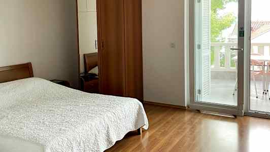 Et soveværelse med dobbeltseng, skab i træ og glasdør, der fører til altanen. (AI-genereret tekst)