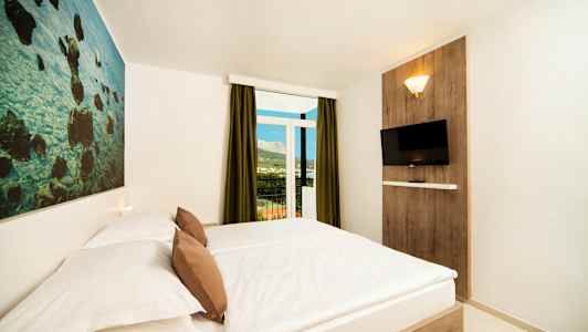 Et hotelværelse med en dobbeltseng, en vægdekoration, et vægmonteret tv og en balkon med udsigt. (AI-genereret tekst)