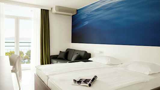 Dobbeltværelse med stort blåt vægmaleri bag sengen. Altan med havudsigt. (AI-genereret tekst)