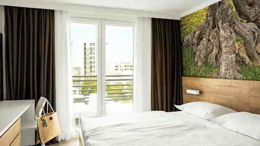 Et hotelværelse med en seng, en skrivebordsstol og et naturmotiv på væggen. (AI-genereret tekst)